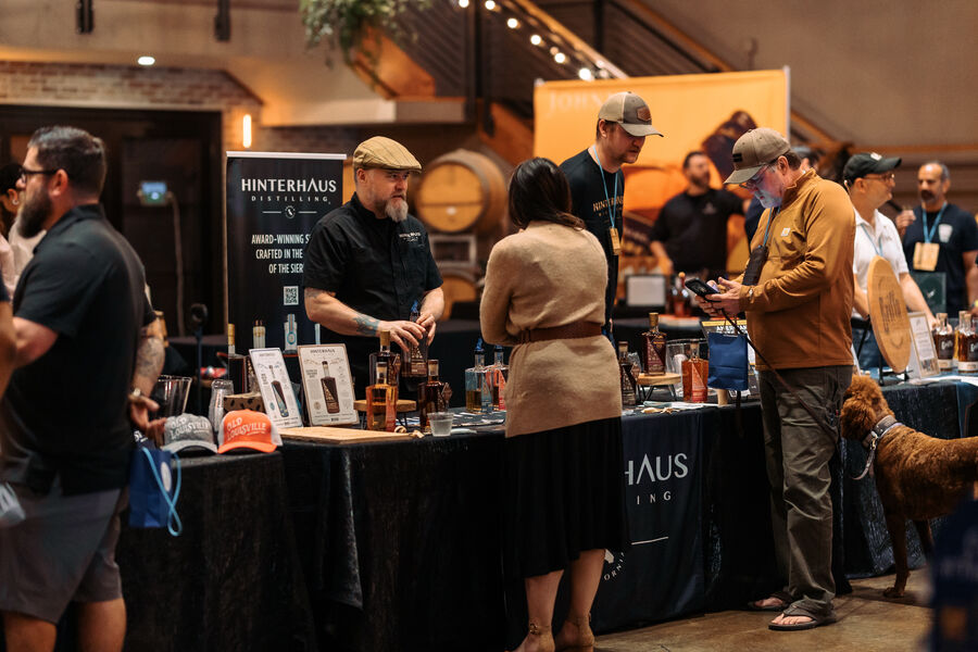 Attendees tasting whisk(e)y and chatting with a distiller at a festival booth