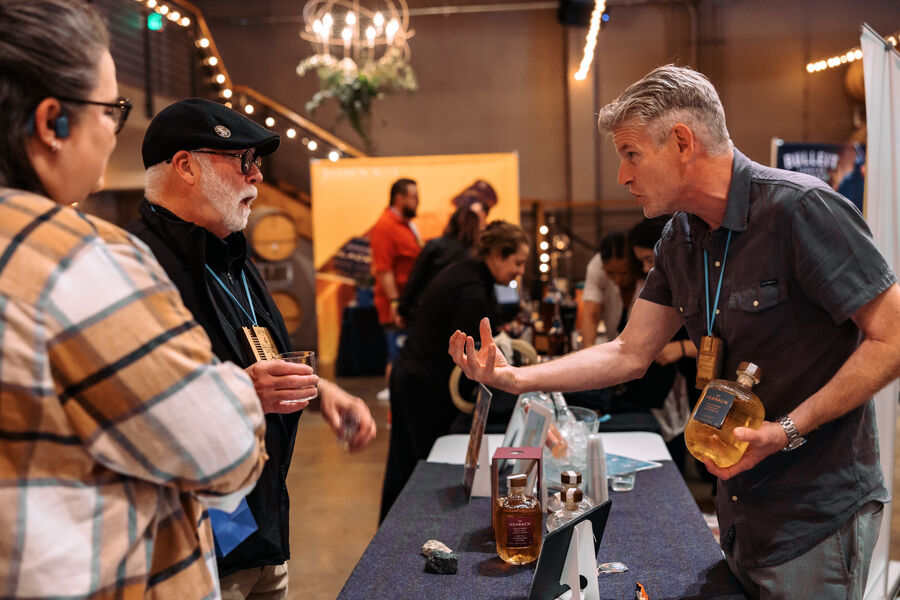 A group of attendees laughing and sampling whisk(e)y near barrel racks
