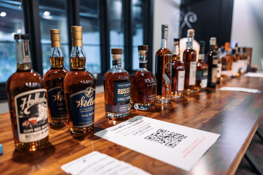 A group of attendees toasting with whisk(e)y bottles in front of barrel racks