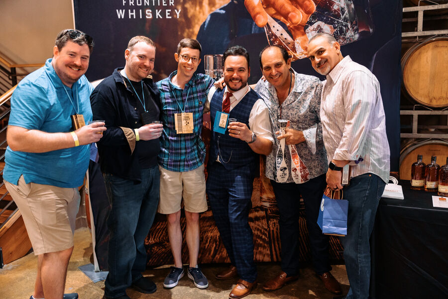 A vendor smiling while pouring a whisk(e)y sample for a guest